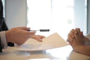 One person handing another person a pen and piece of paper